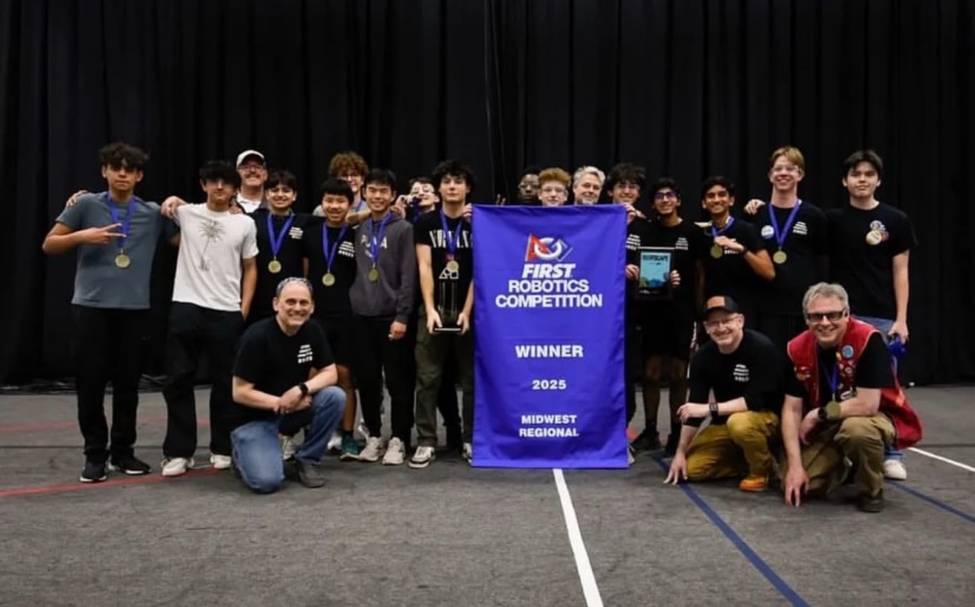 Team 8029 with the FIRST Robotics Competition winner banner for the 2025 Midwest Regional, wearing medals and holding the trophy