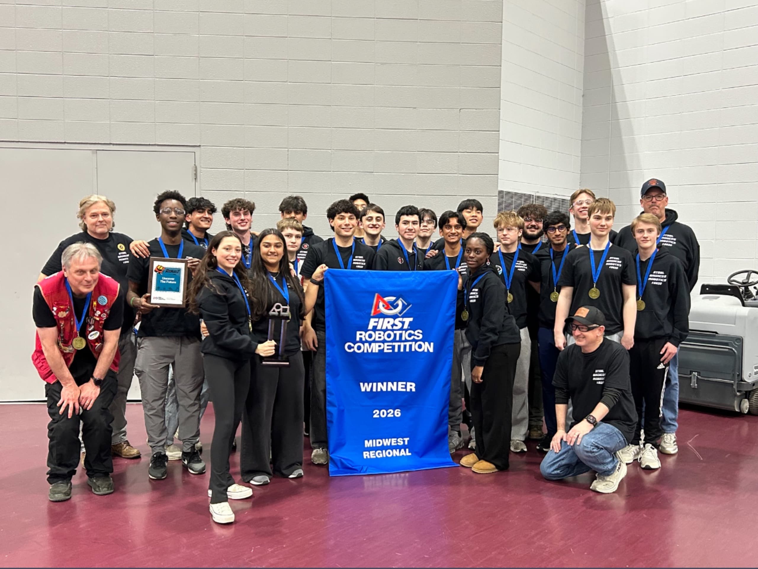 Team 8029 with the FIRST Robotics Competition winner banner for the 2026 Midwest Regional, wearing medals and holding the trophy