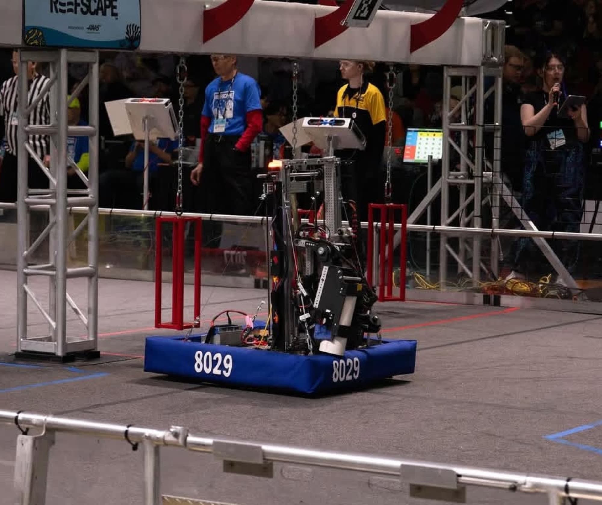 Team 8029's robot on the field during a REEFSCAPE match, its number on the blue bumpers