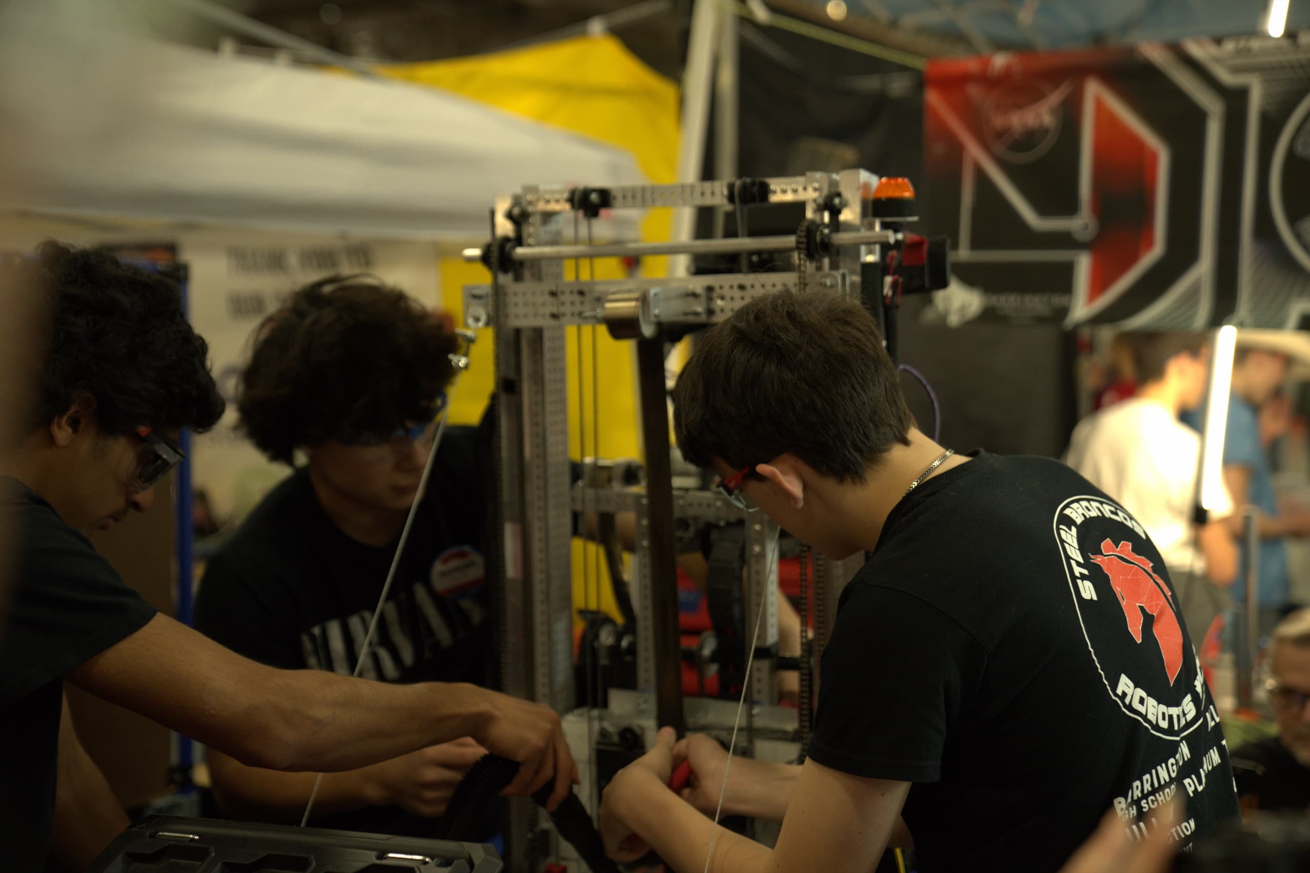 Three Steel Bronco students working together on the robot's mechanism in the pit at competition